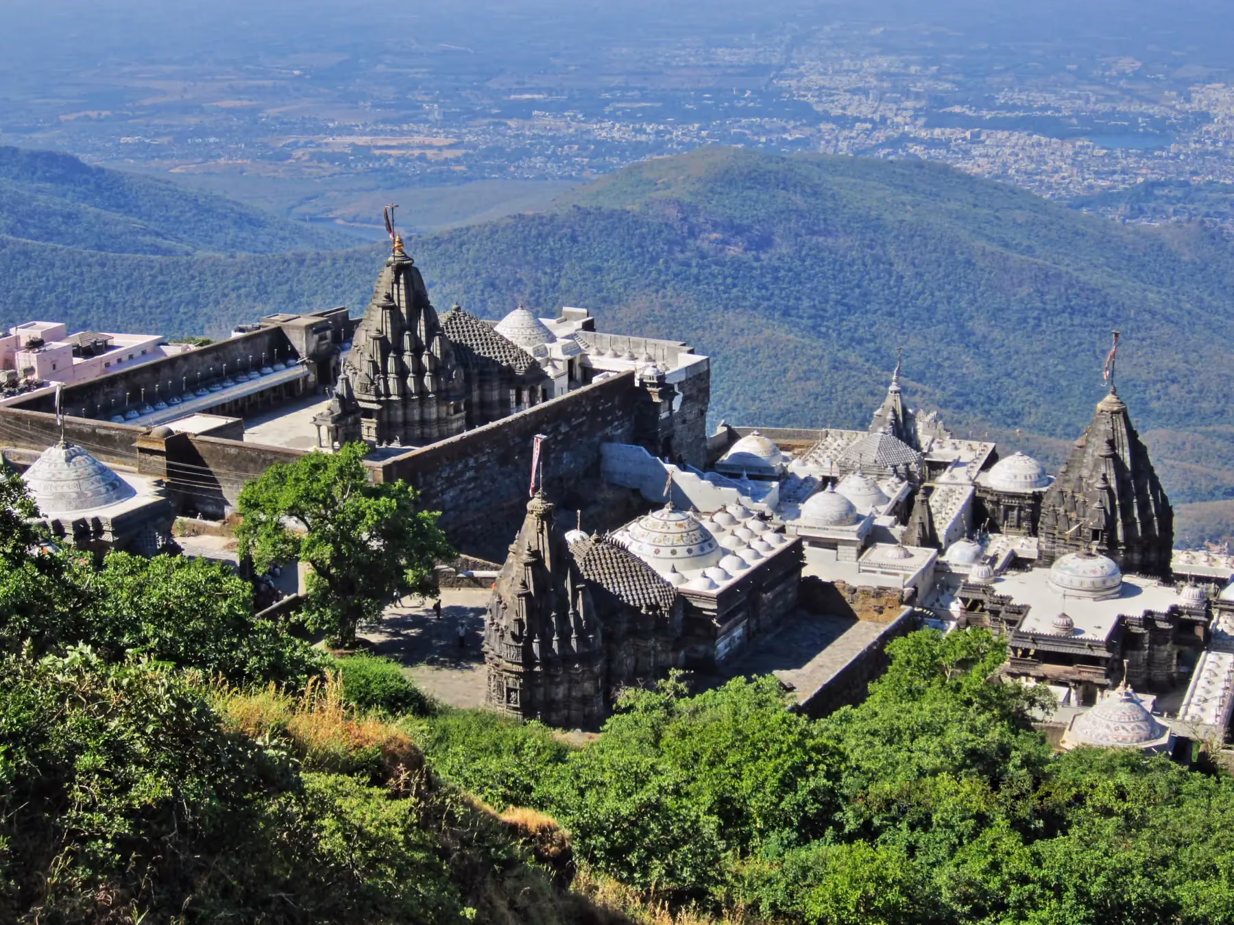 Aerial view of the cluster of Jain temples on Girnar mountain, their white spires set against the hillside